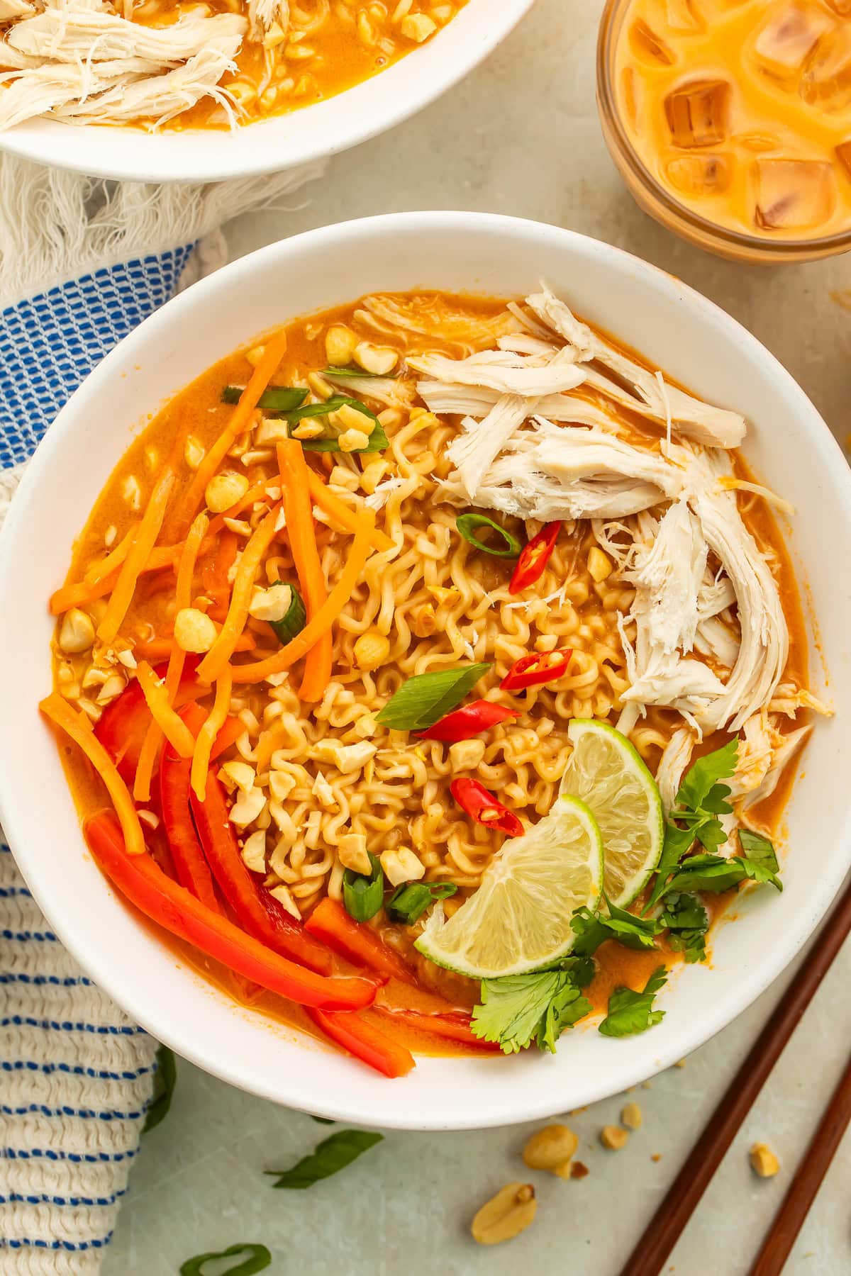 Close up of a bowl of peanut butter ramen topped with shredded carrots, bell peppers, lime wedges and shredded chicken.